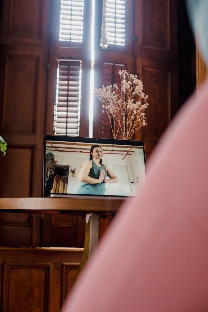 About A woman teaching a yoga class via video on a laptop indoors, with natural light.