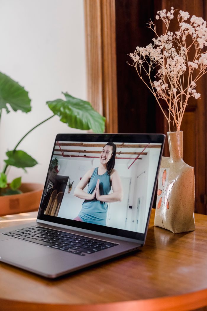 About A woman practices yoga online using a laptop at home.